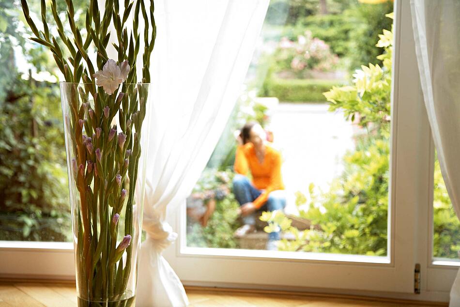 Blick aus dem Fenster in einen Garten, dort gärtnert eine Frau.