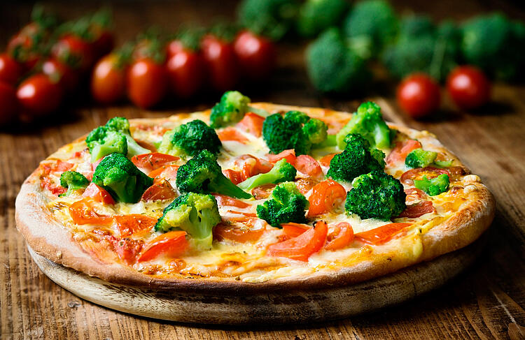 Gemüsepizza mit Broccoli und Tomaten auf einem Holzbrett.