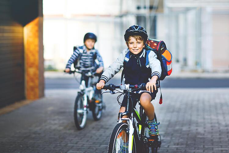 Zwei Jungen mit Schulranzen auf dem Rücken fahren mit dem Fahrrad zur Schule