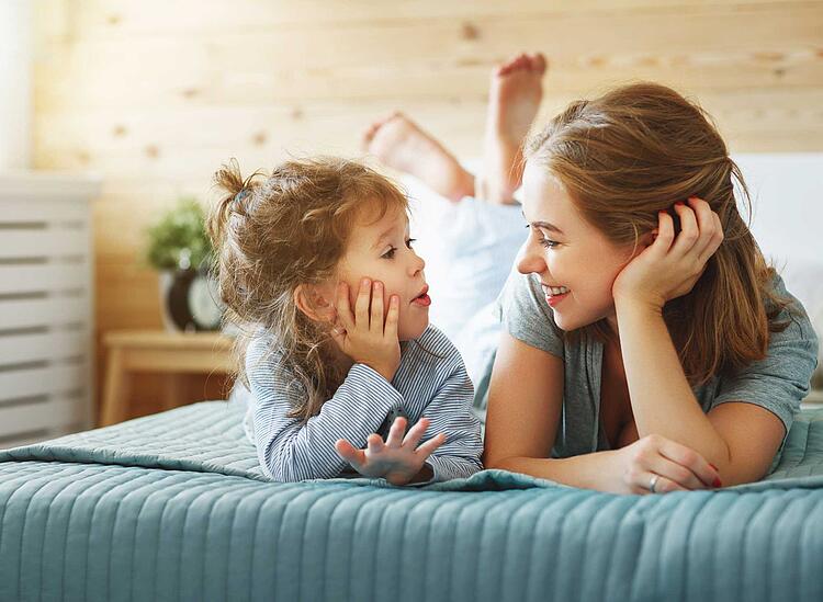 Mutter und Tochter liegen auf dem Bett und lachen zusammen