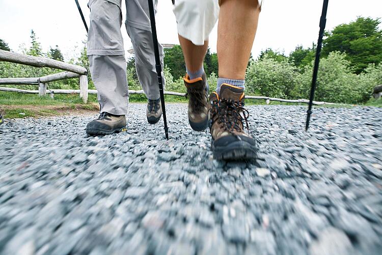 Zwei Menschen beim Nordic Walking auf einem Schotterweg, Ausschnitt Füße mit Wanderschuhen.