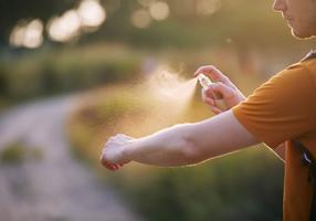Mann sprüht seinen Arm mit einem Spray gegen Insekten ein