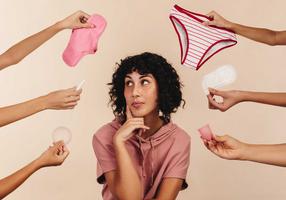 Frau umgeben von Händen, die ihr Menstruationsprodukte entgegenstrecken Frau umgeben von Händen, die ihr Menstruationsprodukte entgegenstrecken