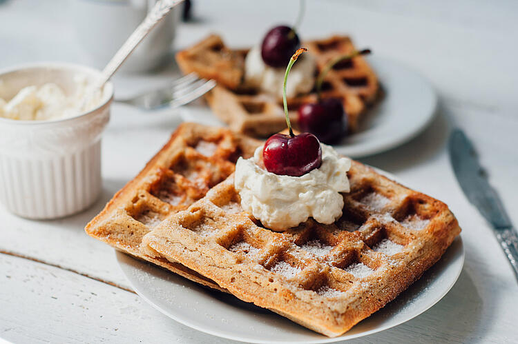 Mandelwaffeln auf zwei Tellern mit Sahne und Kirsche verziert.