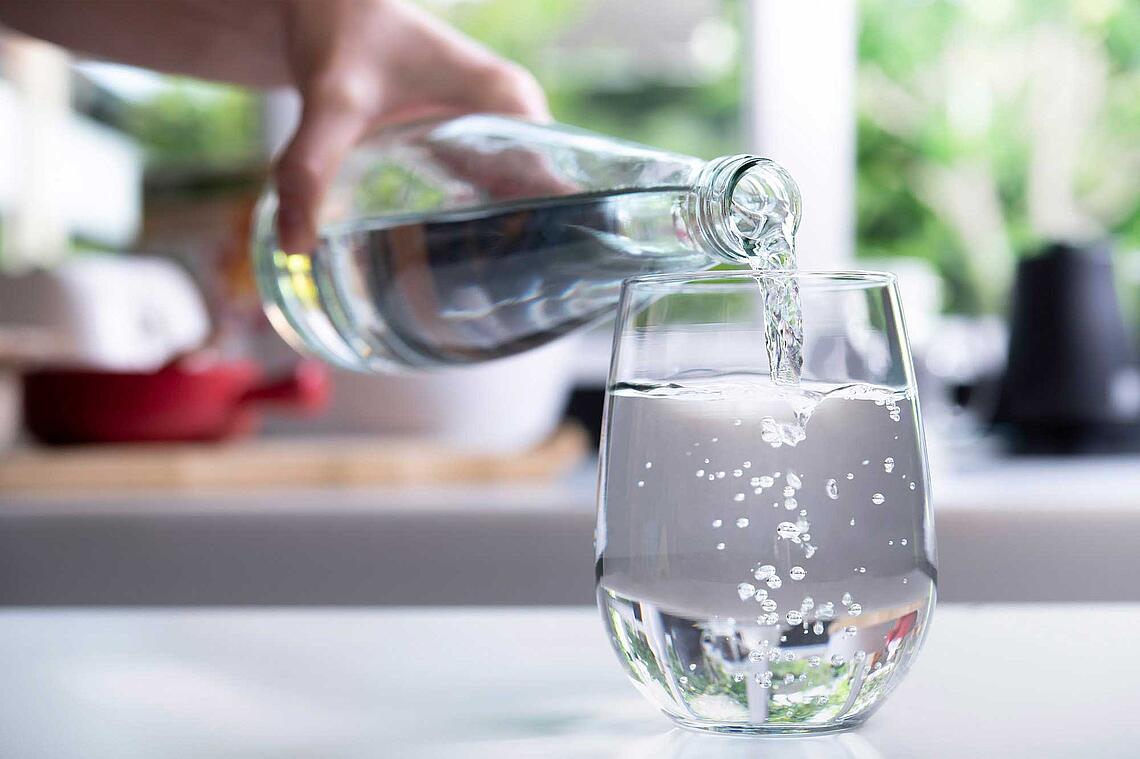 Hand gießt Mineralwasser aus einer Flasche in ein Glas