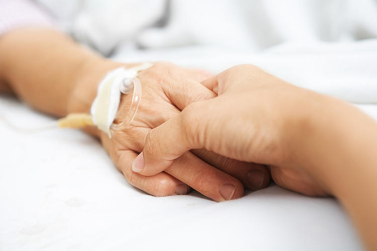 Frau hält die Hand einer Seniorin im Krankenbett.
