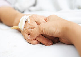 Frau hält die Hand einer Seniorin im Krankenbett.