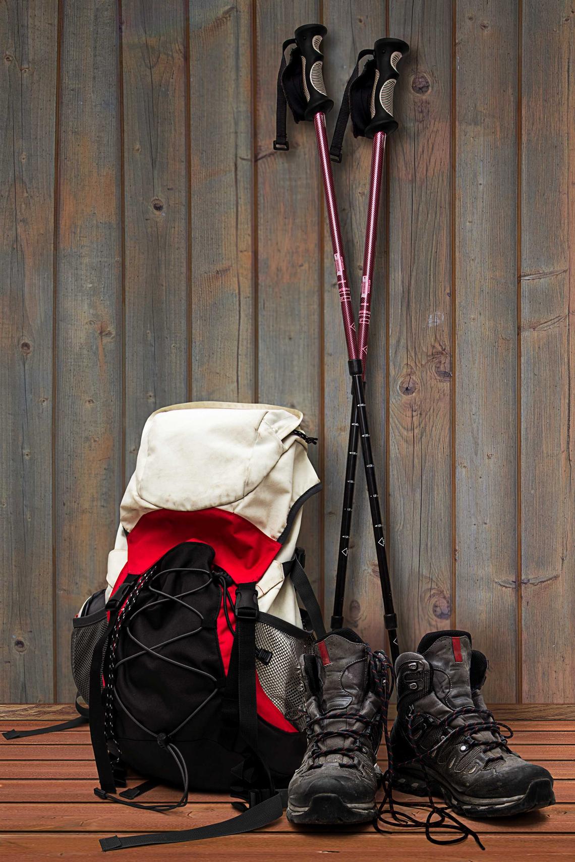 Wanderrucksck, Wanderschuhe und Wanderstöcke lehnen an einer Holzwand