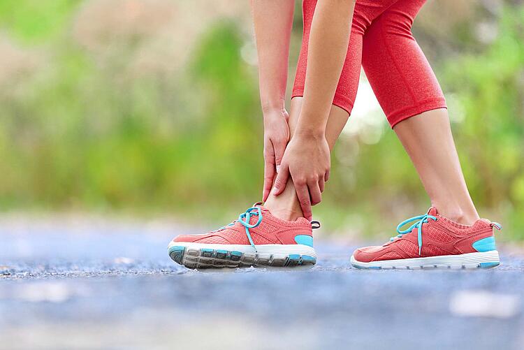 Frau mit Joggingschuhen fasst sich an den Knöchel.