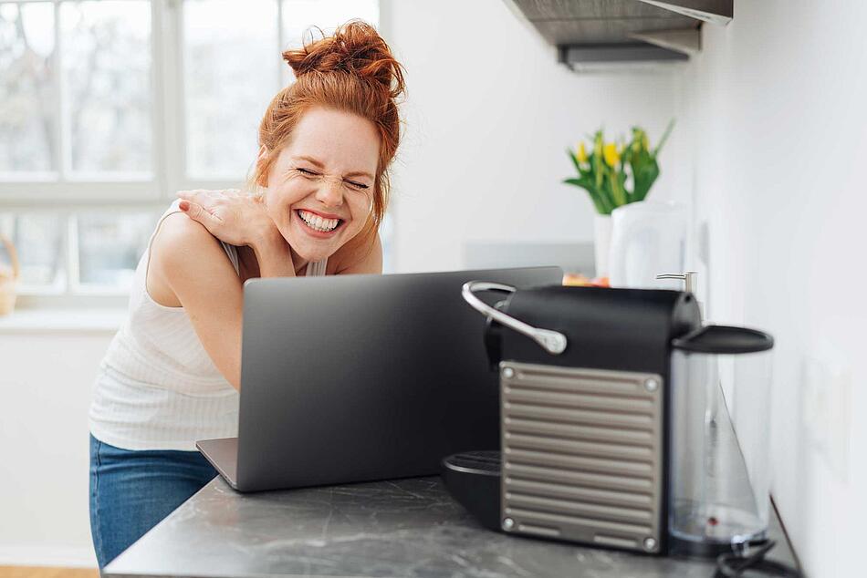 Frau lacht sptizbübisch vor dem Laptop