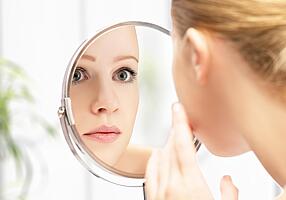 Frau schaut in Kosmetikspiegel