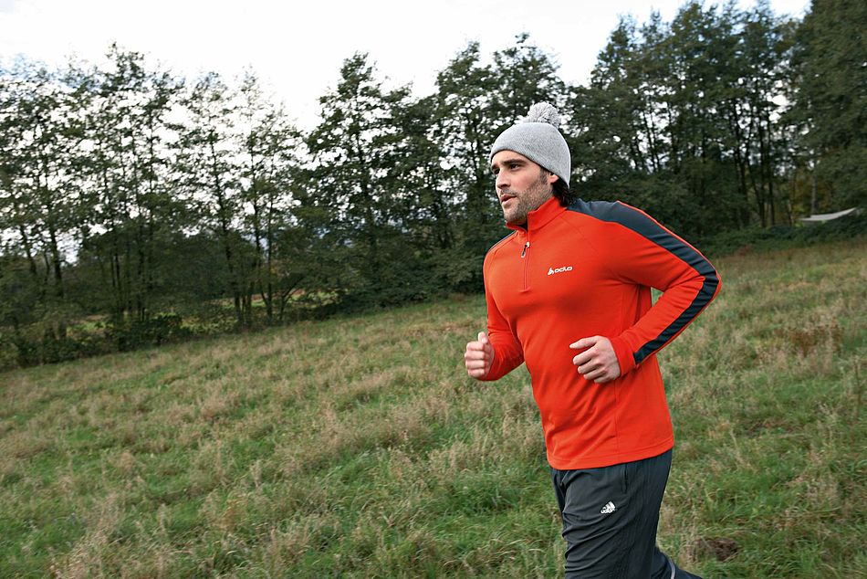 Junger Mann in Sportkleidung mit Strickmütze joggt über eine Wiese mit Bäumen im Hintergrund. - Bildnachweis: © wdv / Jan Lauer Junger Mann in Sportkleidung mit Strickmütze joggt über eine Wiese mit Bäumen im Hintergrund.