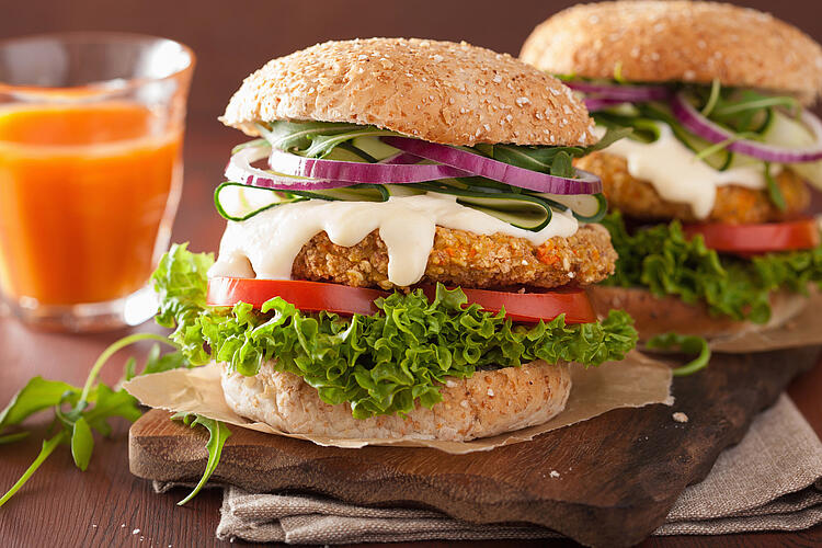 Zwei Burger mit Salat auf Holzbrett, daneben ein Glas Saft.