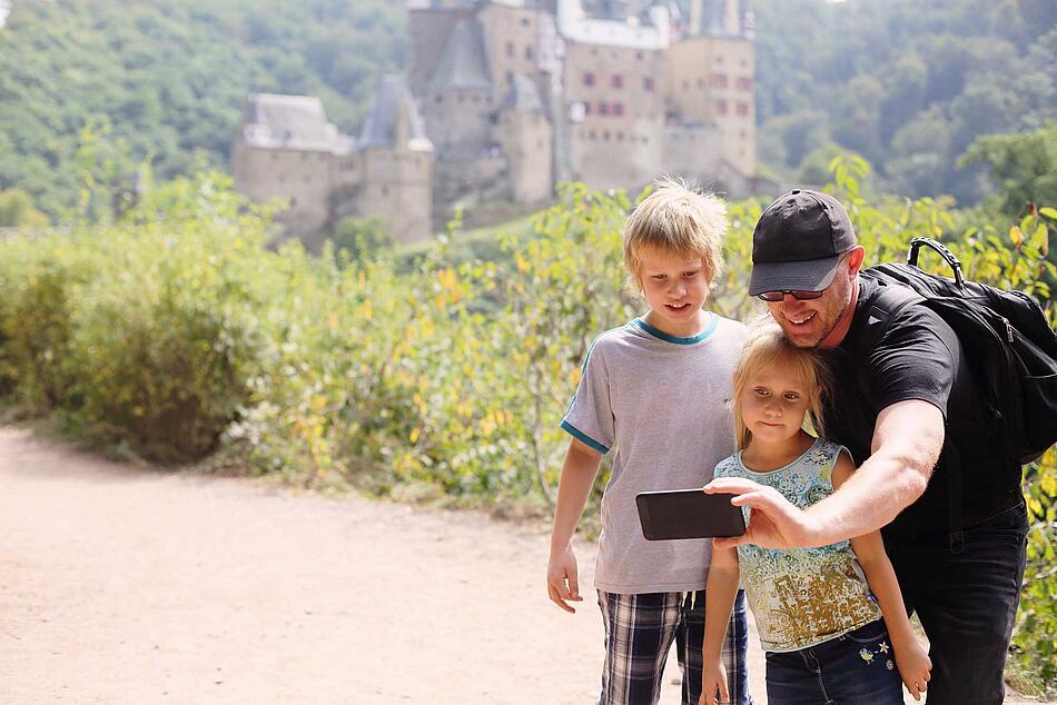 Vater macht mit seinen Kindern ein Selfie vor einem Schloss