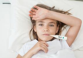 Mädchen liegt mit einem Fieberthermometer im Mund im Bett.