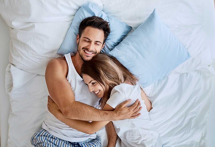 Paar liegt im Bett, umarmt sich und lacht