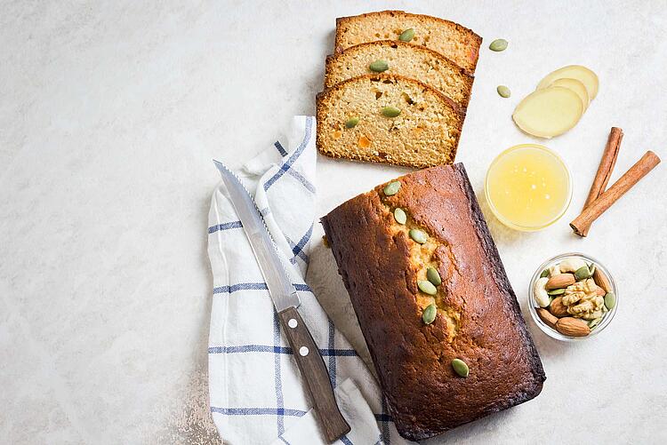 Aufgeschnittener Kuchen in Kastenform mit Kürbiskernen, Zimtstangen und Nüssen.