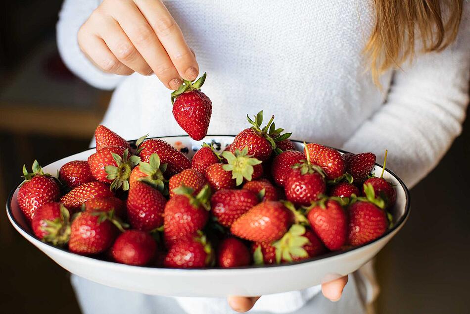 Frau greift in eine Schüssel voller Erdbeeren