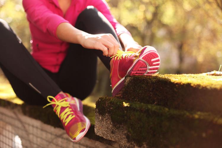 Frau sitzt auf einer Mauer und bindet ihre Laufschuhe