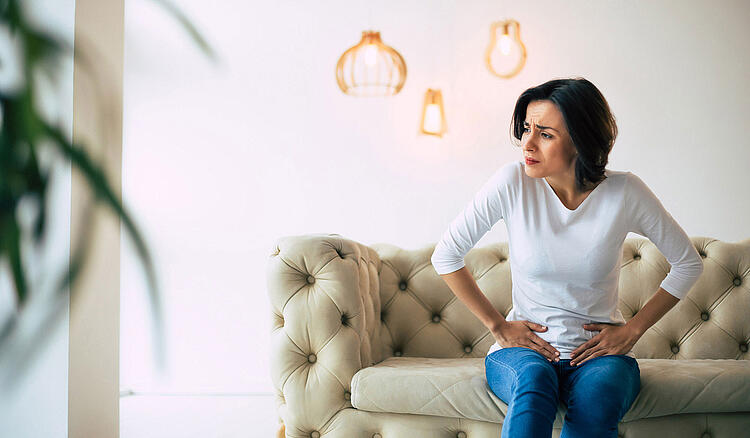 Frau mit Bauchschmerzen sitzt auf dem Sofa.