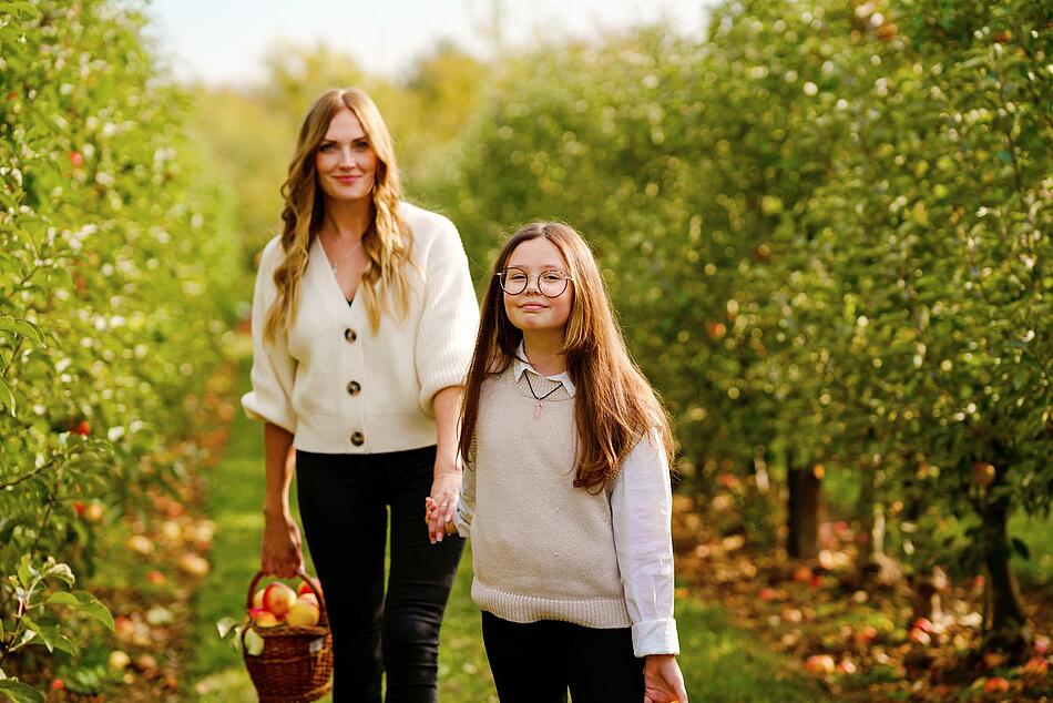 Mutter und Tochter laufen über eine Obstbaumwiese