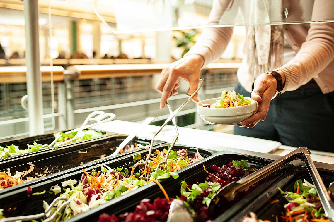 Frauenhände bedienen sich am Salatbuffet in einer Kantine