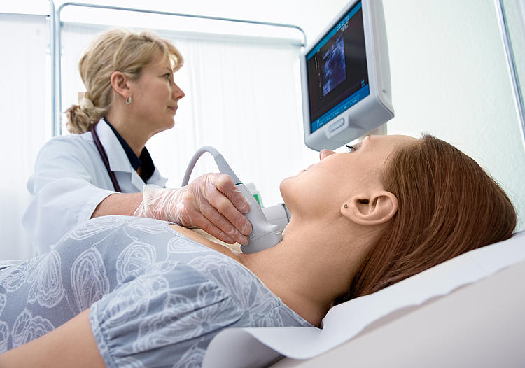 Ärztin untersucht die Schilddrüse einer Frau mit Ultraschall.