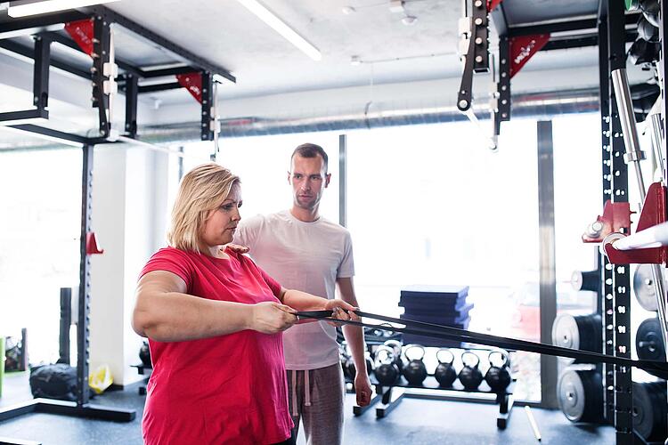 Übergewichtige Frau trainiert im Fitnessstudio unter der Anleitung ihres Trainers.