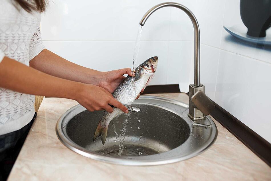 Frau entschuppt einen Fisch unter einem Wasserhahn