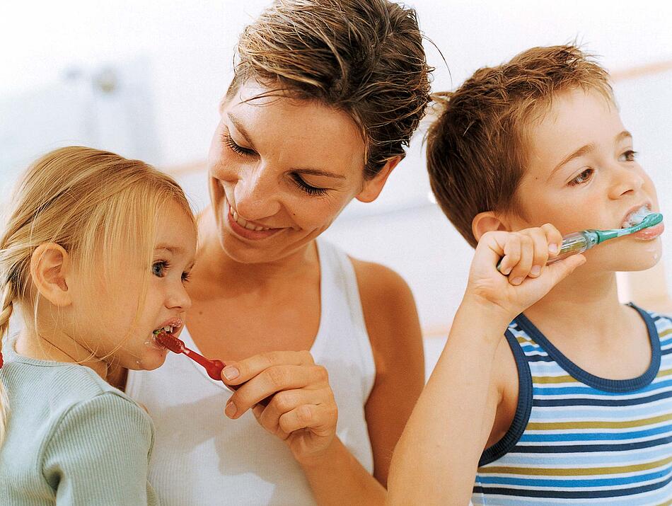 Mutter putzt ihrer Tochter die Zähne, der Sohn putzt selber.