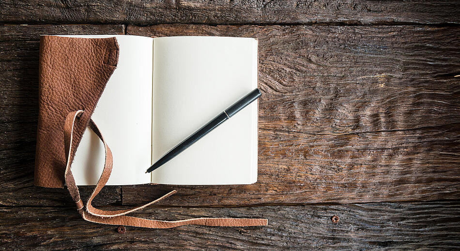 Aufgeschlagenes Notizbuch mit Stift auf einem Holztisch.