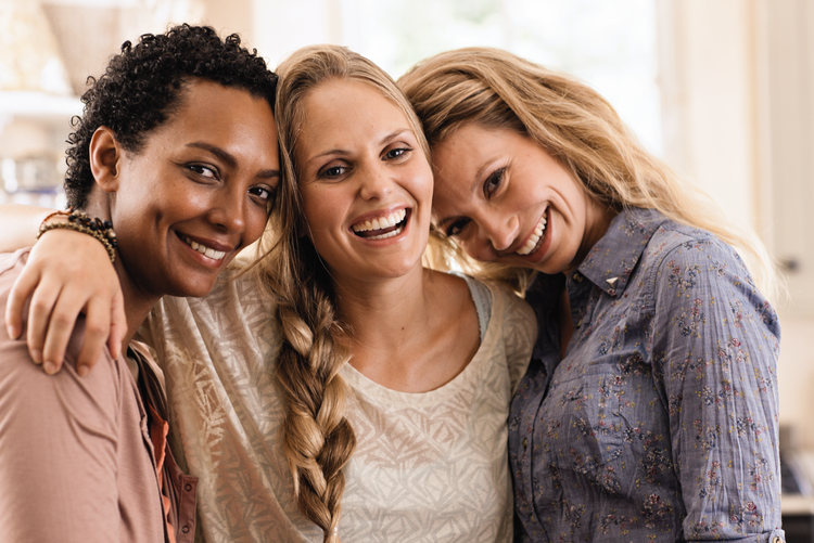 Drei Frauen halten sich im Arm und lachen.