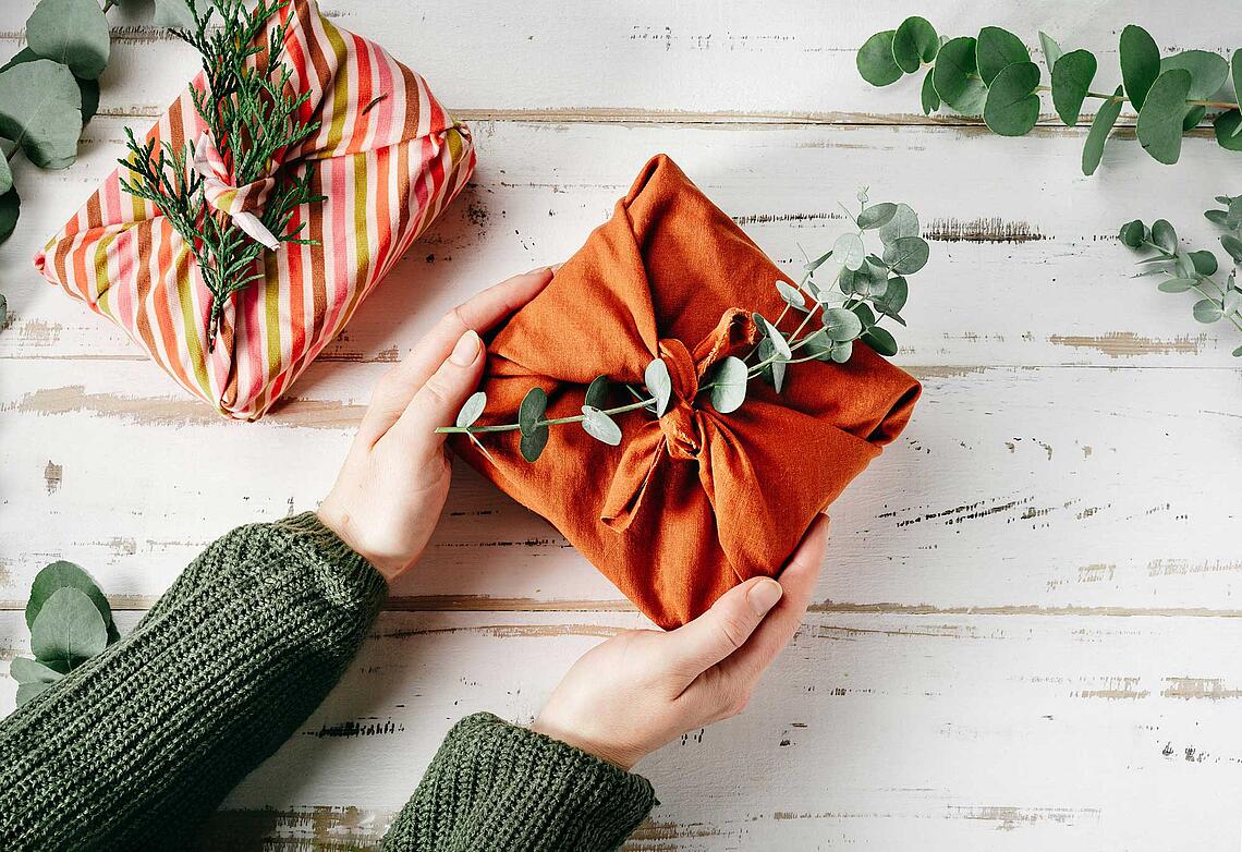 Hände halten ein in ein Tuich eingepacktes Geschenk