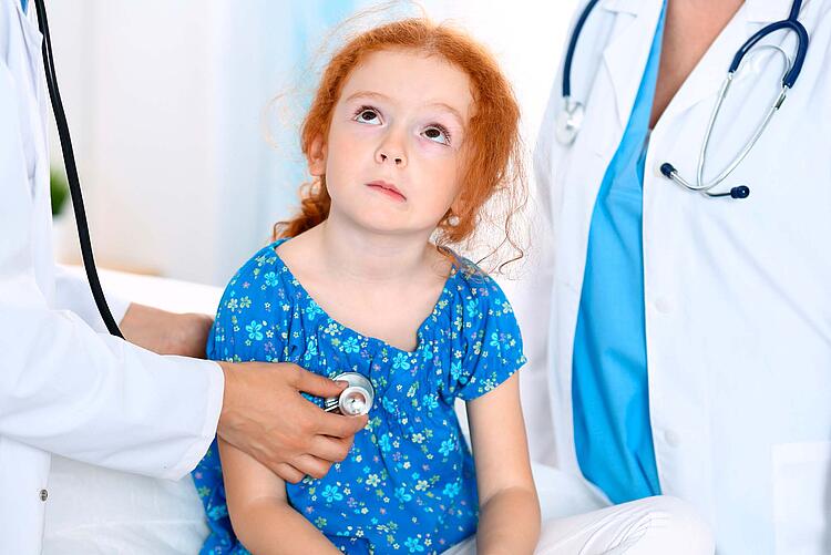 Ein Arzt hört ein kleines Mädchen mit dem Stethoskop ab.