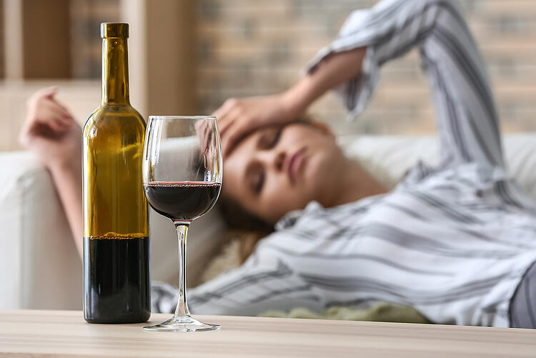 Frau liegt auf der Couch vor sich eine halb leer getrunkene Flasche Wein.