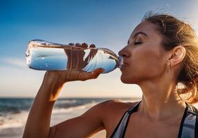 Frau trinkt bei warmem Wetter Wasser aus der Flasche