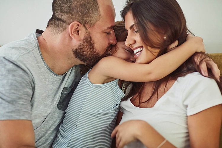 Bildnachweis: © gettyimages.de / PeopleImages Eltern kuscheln mit ihrer Tochter.