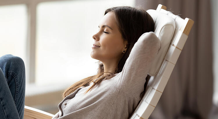 Bildnachweis: © istockphoto.com / fizkes Junge Frau sitzt mit geschlossenen Augen entspannt in einem Schaukelstuhl.
