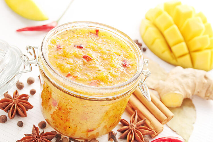 Mango-Chutney im Glas, daneben eine frische Mango, Ingwer und Gewürze.