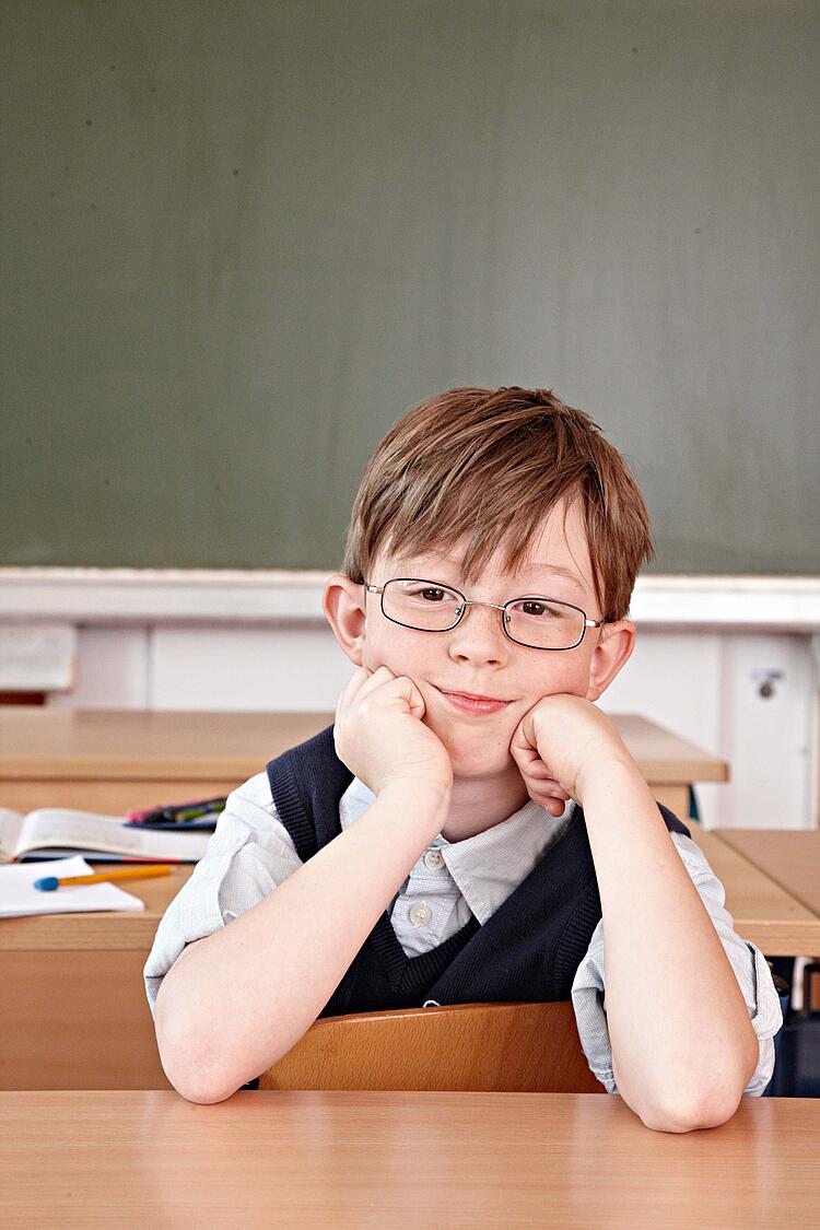 Junge sitzt im Klassenzimmer am Tisch.