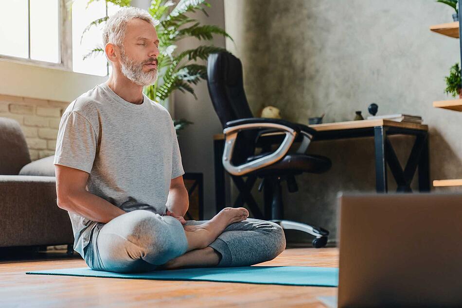 Mann macht Yoga vor dem Schreibtisch