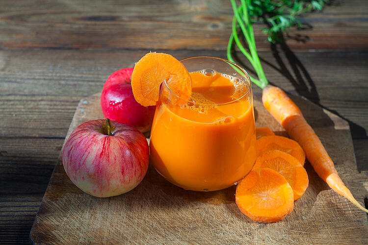 Apfel-Möhren-Drink in einem Glas mit Karotten und Äpfeln auf einem Holztisch.
