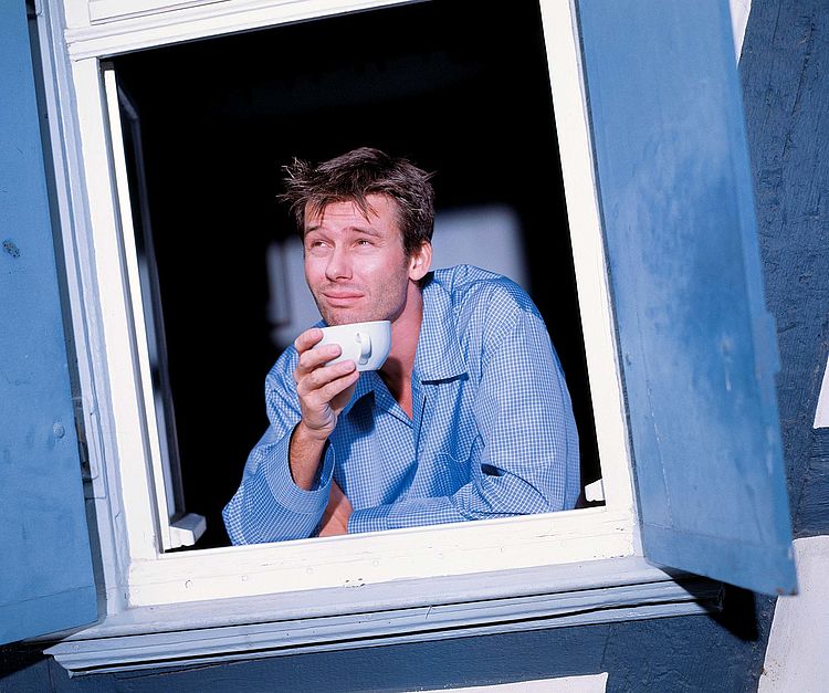Bildnachweis: © wdv / Frank Blümler Mann im Schlafanzug mit einer Tasse Kaffee in der Hand schaut aus dem Fenster.