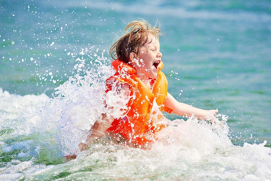 Junge mit Schwimmweste planscht im Wasser