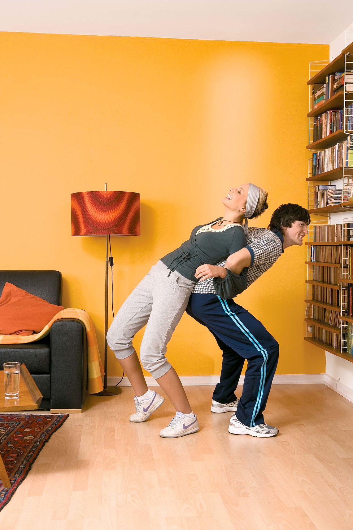 Bildnachweis: © wdv / Michael Völler Lachendes junges Paar macht im Wohnzimmer gemeinsam Gymnastikübungen zum Rückenstretching.
