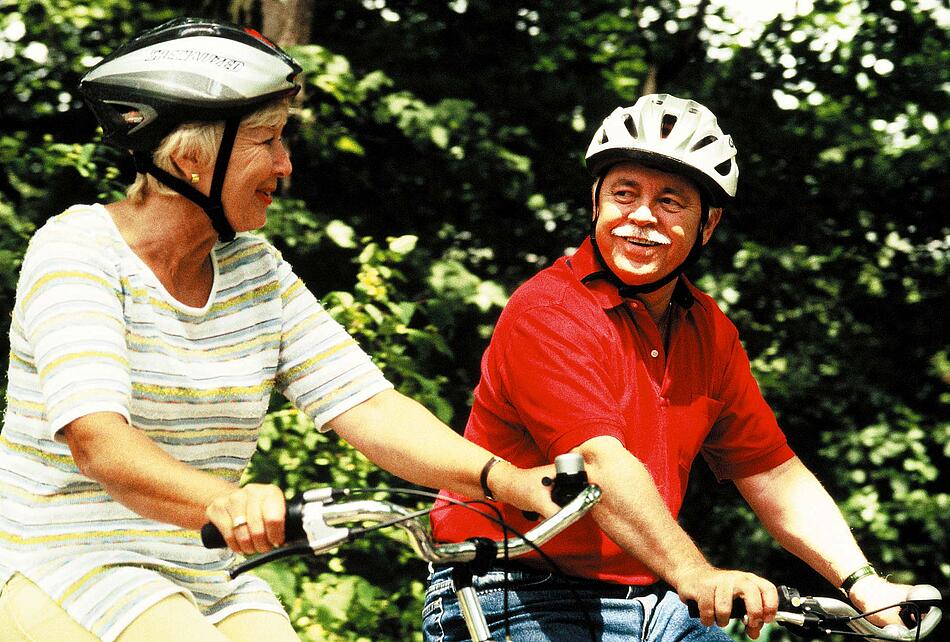 Älteres Paar mit Fahrradhelmen beim Radfahren im Wald.