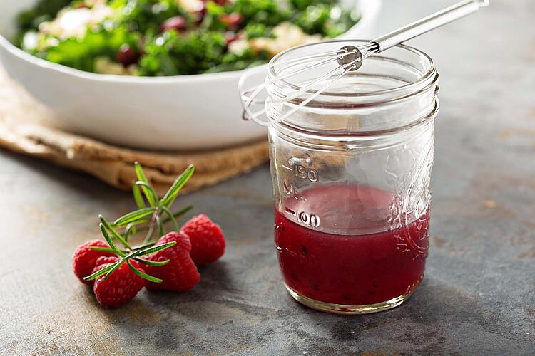 Himbeer-Balsamico-Dressing im Glas darauf liegt ein Schneebesen.