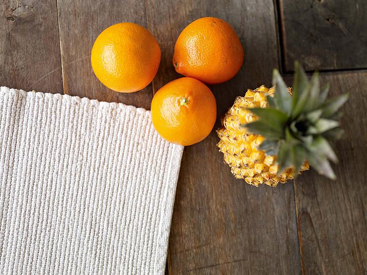 Drei Orangen und eine Ananas auf einem Holztisch.