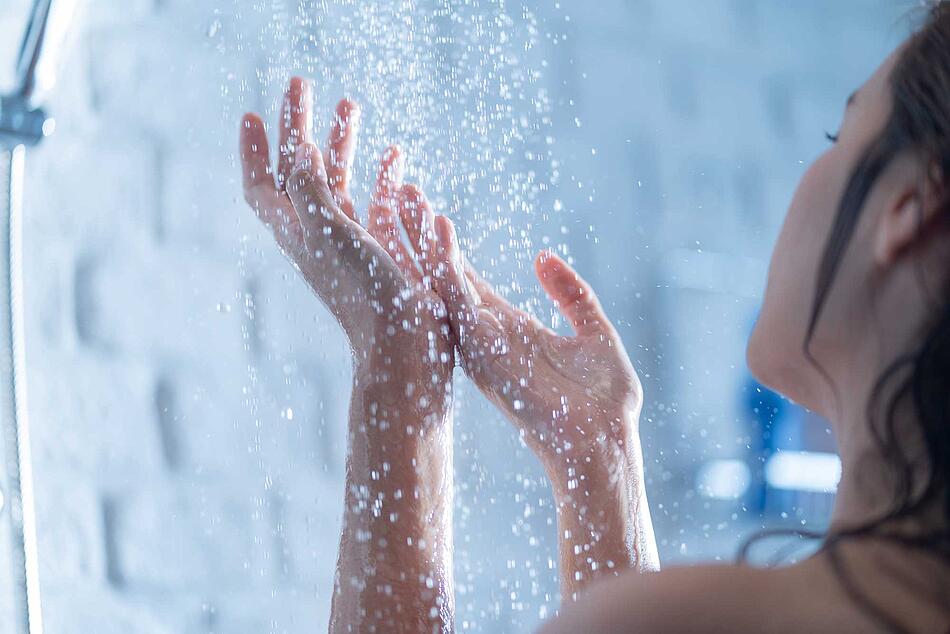 Eine Frau hält ihre Hände unter den Wasserstrahl einer Dusche