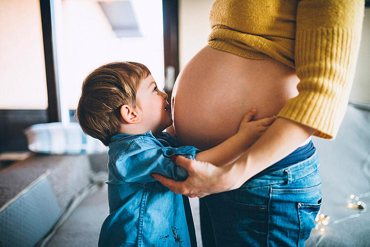 Kleiner Junge umarmt den Bauch der hochschwangeren Mutter